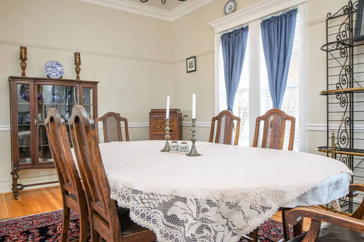A formal dining room featuring a large wooden dining table adorned with a lace tablecloth, elegant candlesticks, and a china cabinet in the background. The decor evokes a sense of history and warmth, perfect for festive gatherings and intimate meals.