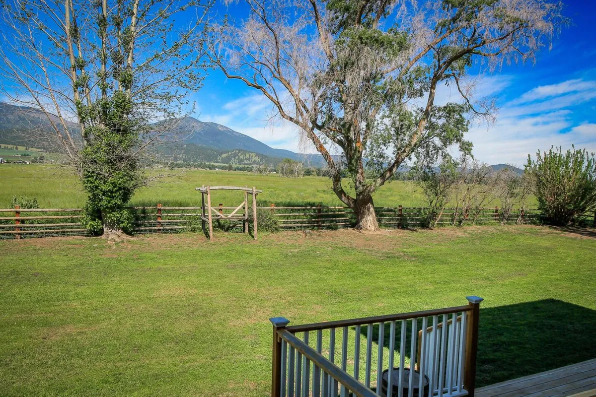 A vibrant green lawn dotted with a large shade tree and a playground structure sits in front of a dramatic mountain vista. The open yard offers ample space for relaxation, gatherings, or play, while the mountains reinforce the scenic connection.