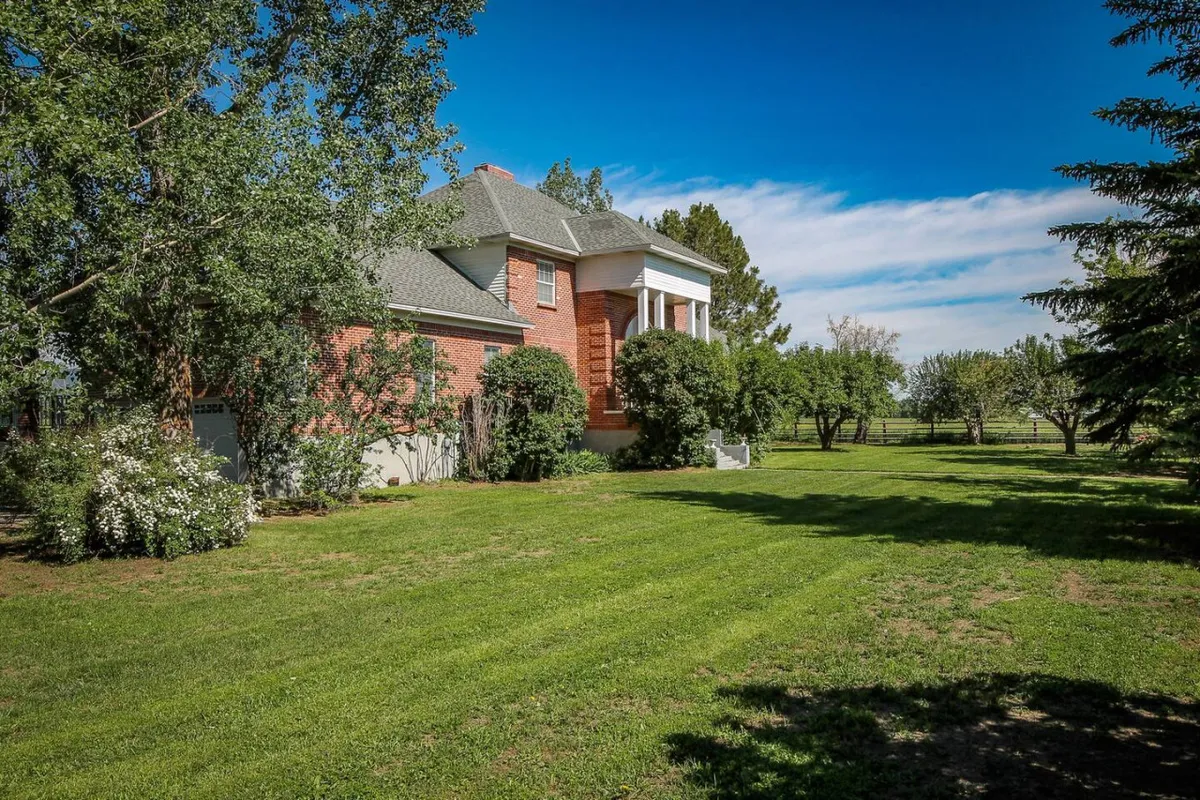A wide shot of the red brick house surrounded by a lush green lawn, mature trees, and flowering shrubs. The expansive grassy area in front is ideal for outdoor games and social gatherings, perfectly capturing the home's inviting ambiance.