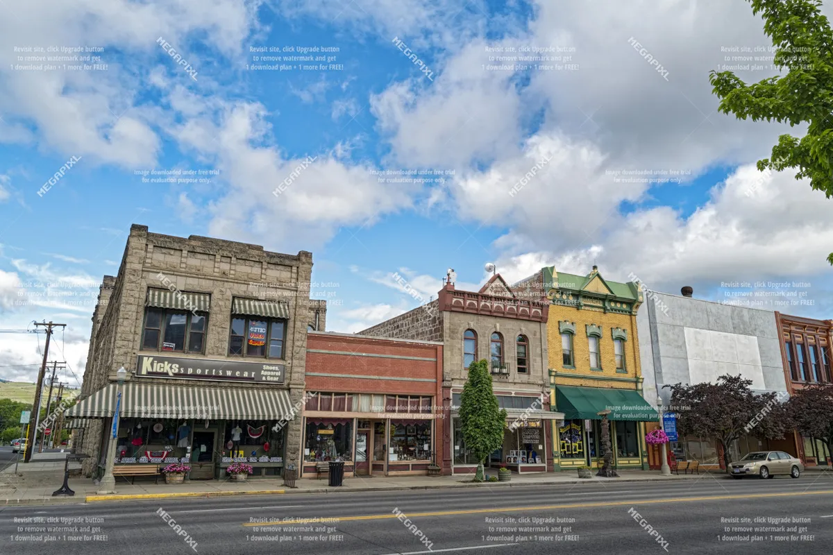 A lively and colorful scene of Baker City's downtown, highlighting storefronts with awnings, local shops, and street trees. The presence of people shopping, strolling, and dining adds vibrancy, linking perfectly to mentions of exploring historic downtown and local culture.