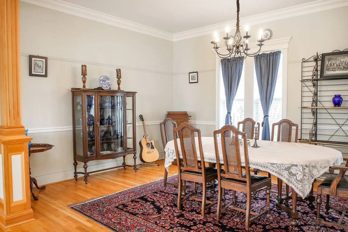 An interior look at the cozy dining area with a large table, elegant chandelier, display cabinet, guitar, and inviting window treatments. The setting is ready for family dinners, celebrations, or music-filled gatherings, emphasizing a welcoming and communal atmosphere.